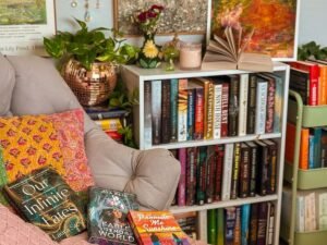 Cozy BookTok-inspired reading nook with fairy lights, floating bookshelves, papasan chair with throw blanket and pillows, and a wall of colorful books.